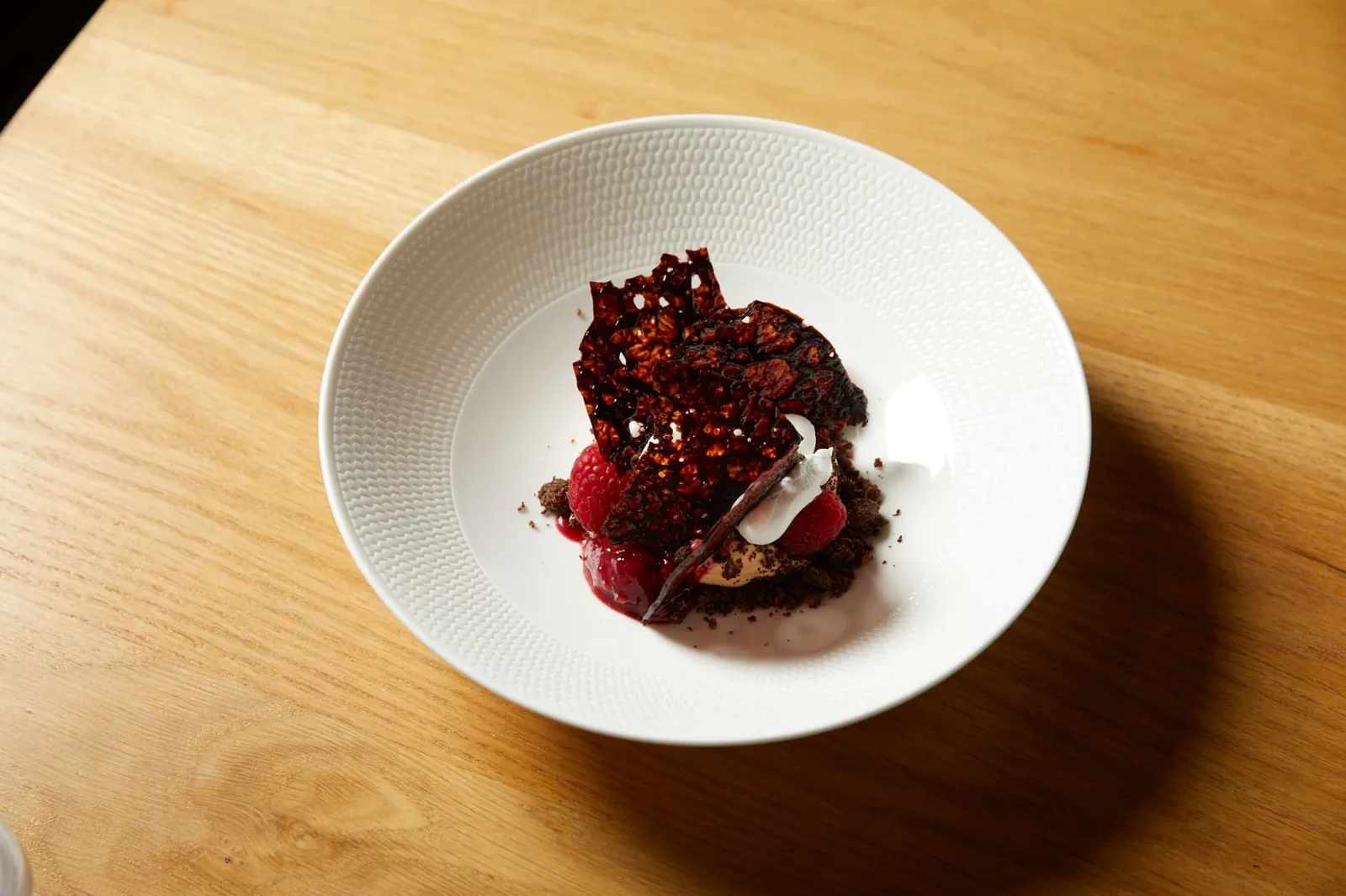 Chocolate dessert with raspberries, whipped cream and a caramelised nut brittle in a white bowl.
