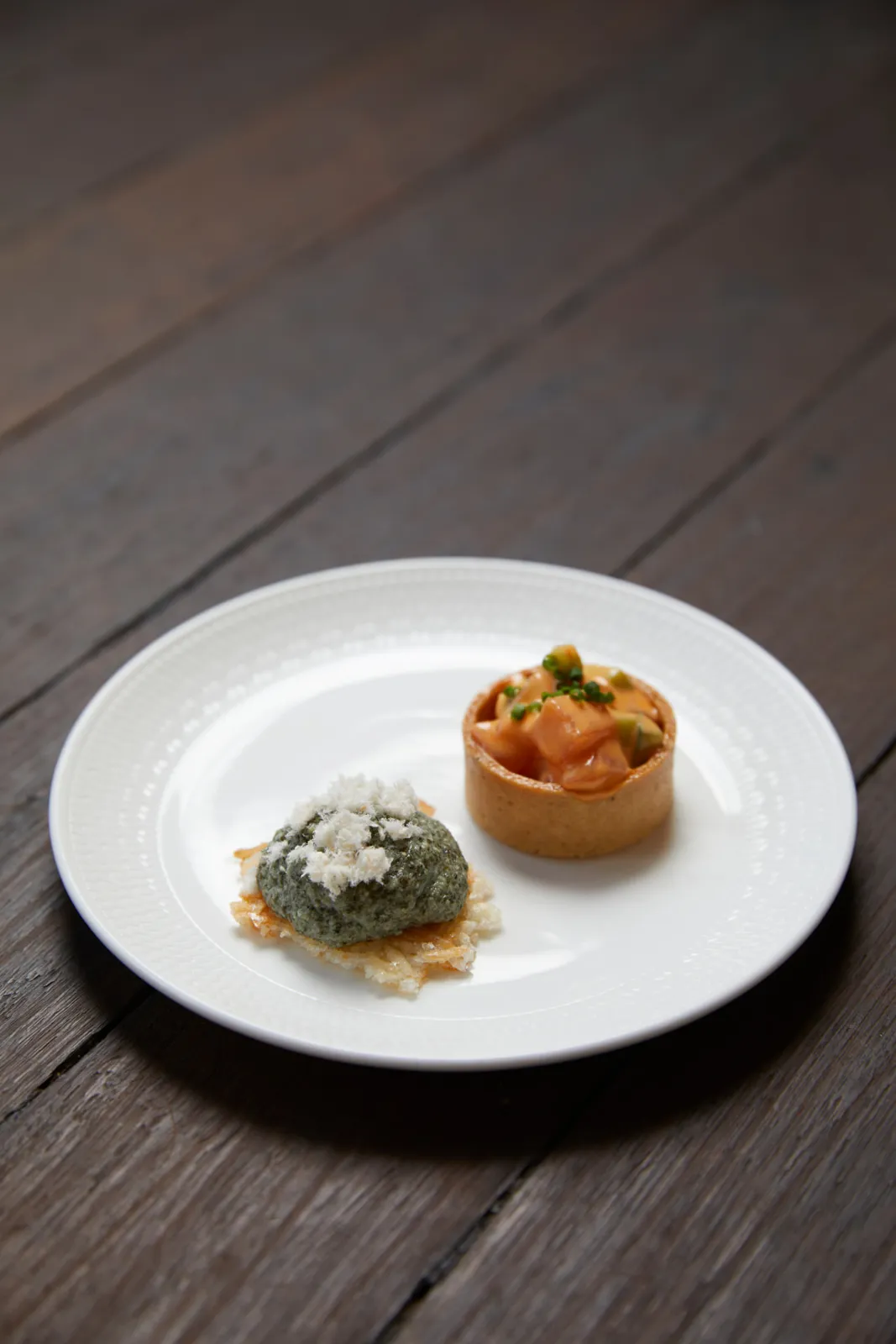 Two canapés on a white plate — herbed mousse on a crisp and a prawn tartlet.