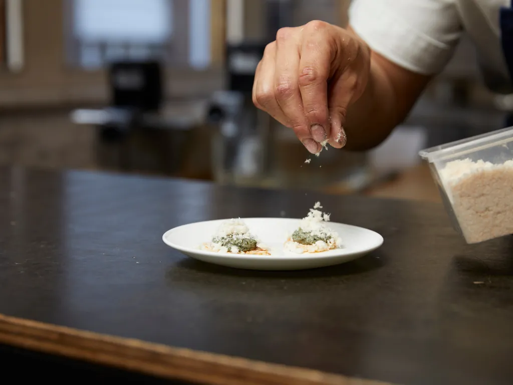 A chef's hand finishing a plate in the kitchen, styled for client entertaining in a corporate setting.