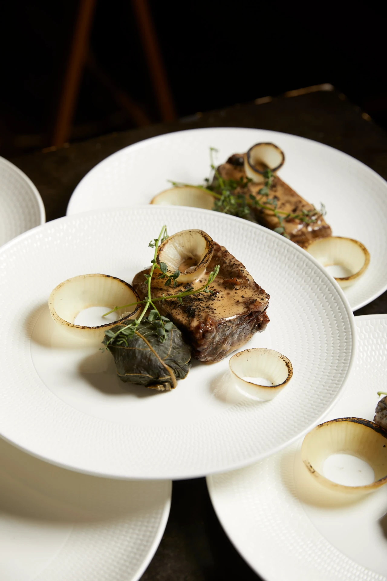 Braised beef with charred onion, thyme and a vine leaf parcel, plated for service.