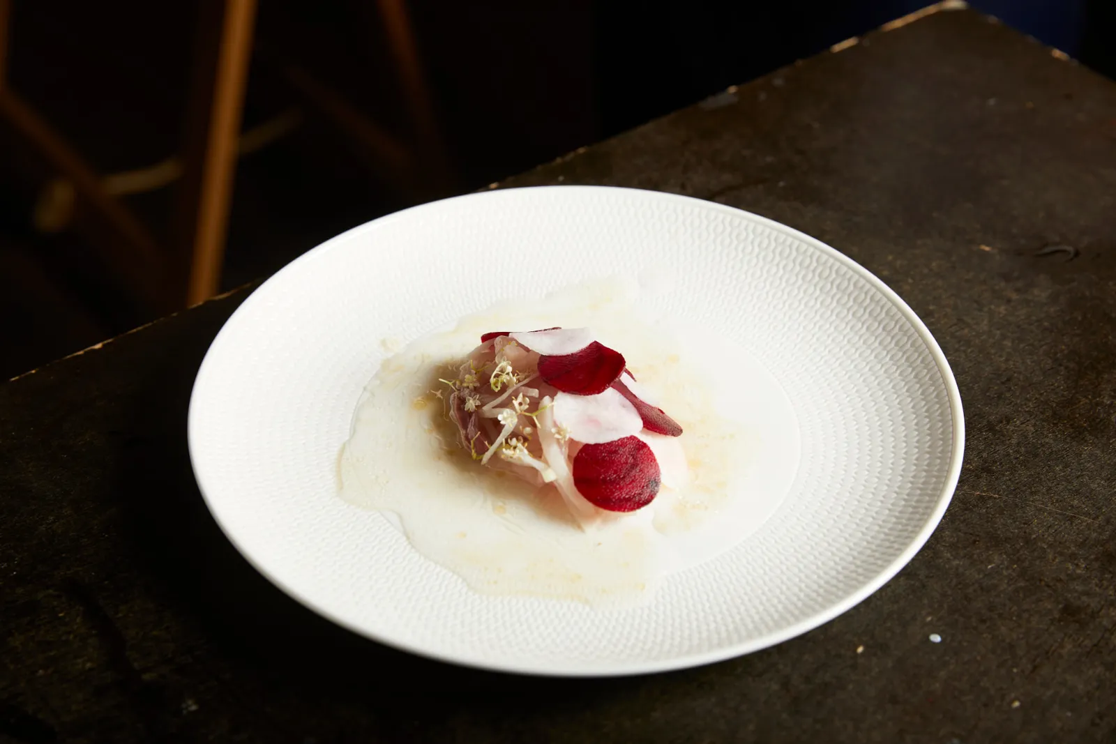 Cured kingfish with beetroot, radish and elderflower in a shallow white bowl.