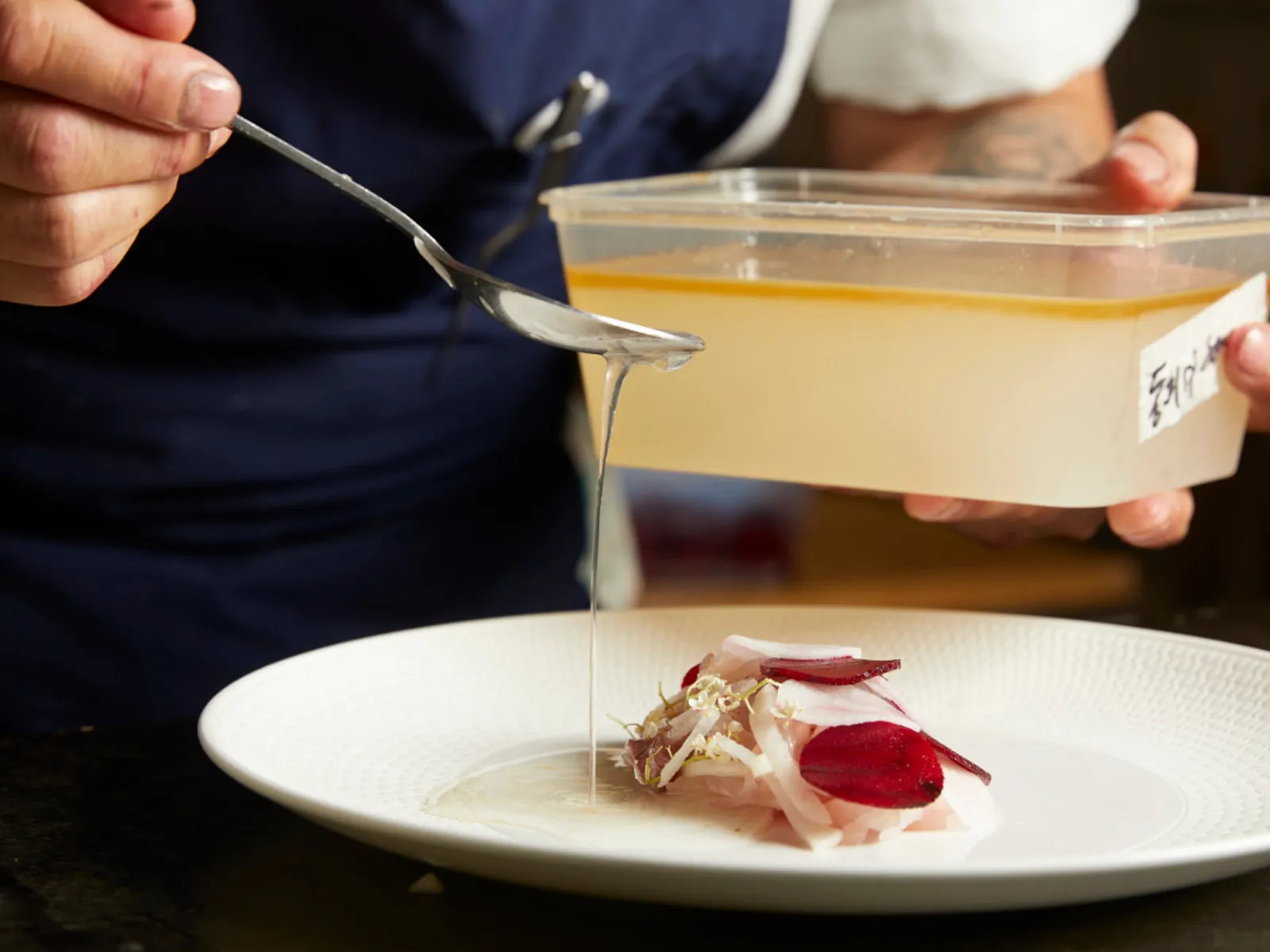 Chef drizzling a finishing sauce over a plated dish, styled for a brand activation or product launch event.